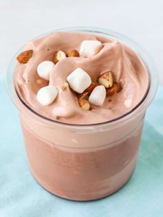 a dessert in a glass with marshmallows and nuts on top, sitting on a blue surface