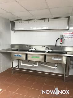 an industrial kitchen with stainless steel sinks and overhead lighting above the sink is tiled walls