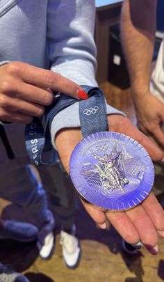 a person holding a purple medal in their hand with other people standing around and looking at it