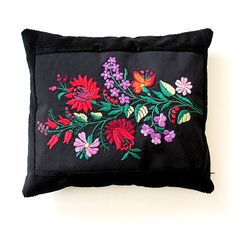 a black pillow with colorful flowers and butterflies embroidered on the front, sitting against a white wall