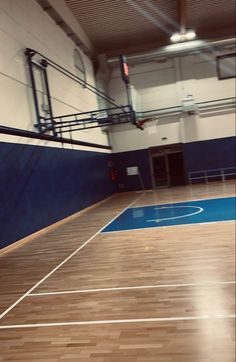 an indoor basketball court with hard wood flooring and blue paint on the side wall