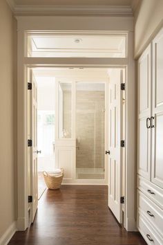 an empty hallway leading to a bathroom with wooden floors and white cabinets on either side