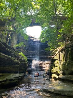 some people are standing in the water under a bridge with a waterfall coming out of it