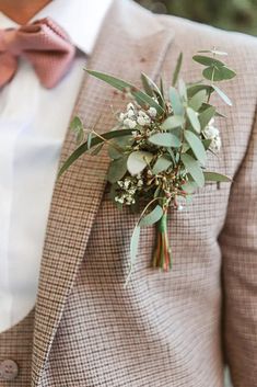 a man wearing a suit and tie holding a boutonniere with greenery on it