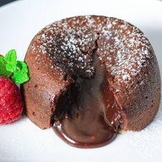 a piece of chocolate cake on a white plate next to a raspberry and mint sprig