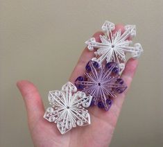 three paper snowflakes in the palm of someone's hand with beads on them