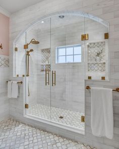 a bathroom with white tile and gold trim on the shower door, windows, and towels