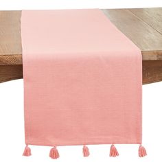 a pink table runner with tassels on the end and a wooden table in the background