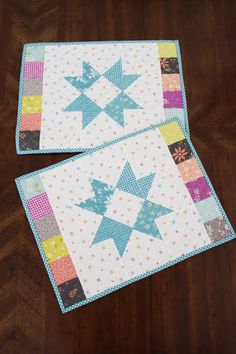 two quilted placemats sitting on top of a wooden table