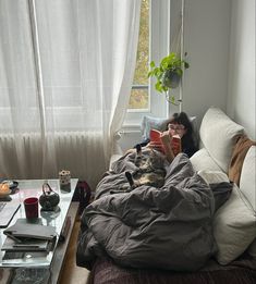 a woman sitting on a couch reading a book with a cat laying on her back