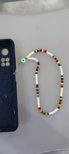 a cell phone with a beaded necklace on it next to a plastic case that has beads attached