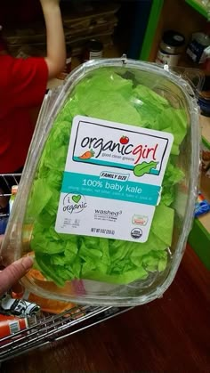 a plastic container filled with lettuce sitting on top of a table next to a person