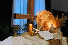 an open book on a table next to a cross and some candles in front of a window