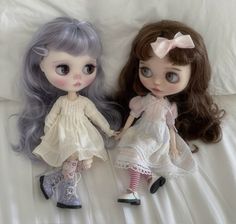 two dolls sitting next to each other on a bed