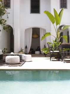 an outdoor living area with a pool and patio furniture in front of a large white house