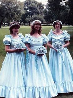 three women dressed in blue dresses standing next to each other on a grass covered field