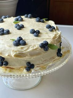 a cake with white frosting and blueberries on top sitting on a glass plate