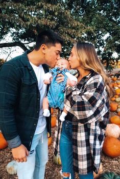 a man and woman holding a baby in front of pumpkins