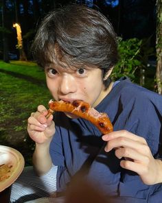 a young man eating a hot dog at an outdoor table