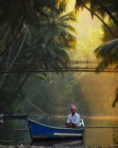 a man sitting in a blue boat on the river with palm trees and bridge above him