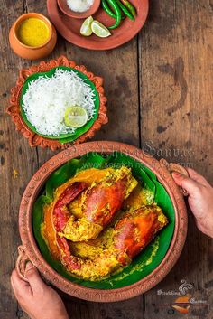 two hands holding a plate with cooked lobsters and rice on the table next to other dishes