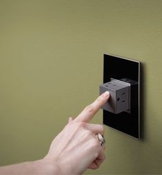 a person is pointing at an electrical outlet on the wall with their finger in it