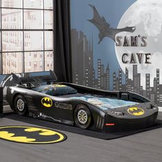 a child's batman car bed is shown in front of a cityscape