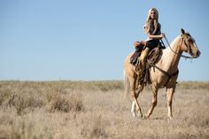 a woman riding on the back of a brown horse across a dry grass covered field