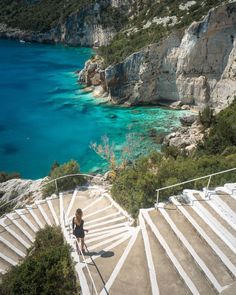 a woman is standing on some steps near the water and cliffs with blue water in the background