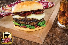 a cheeseburger with bacon and lettuce on a cutting board next to a glass of beer