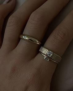 a woman's hand with two gold rings on top of her finger and one diamond ring