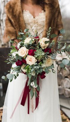 a woman in a wedding dress holding a bridal bouquet with roses and greenery