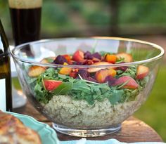 a glass bowl filled with salad next to a bottle of beer