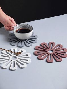 a person holding a coffee cup over a white table with four flower shaped coasters