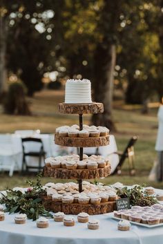 a table topped with lots of cupcakes covered in frosting next to trees