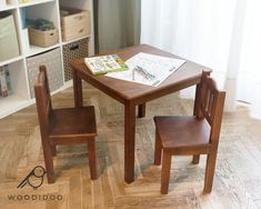 a wooden table with two chairs and a book on it in front of a window