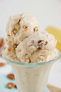 two scoops of ice cream in a glass bowl with nuts on the table next to it