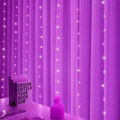 a purple room with white lights on the curtains and a pink candle next to it