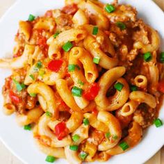 a white plate topped with pasta covered in sauce and green onions on top of a wooden table