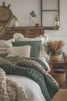 a bed covered in lots of pillows and blankets next to a table with flowers on it