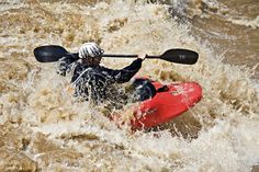 a man riding on top of a red kayak in the water with white caps