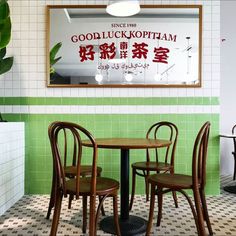 a restaurant with green tile walls and wooden chairs around a small round table in front of a sign that says good luckpham