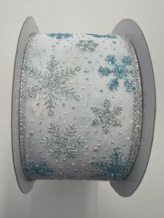 a spool of white and blue ribbon with silver snowflakes on the side