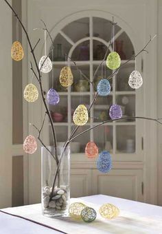 a vase filled with eggs sitting on top of a table next to a tree branch