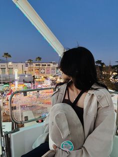 a woman sitting on top of a boat next to a ferris wheel at night with buildings in the background