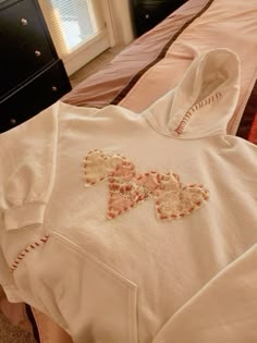 a white hoodie laying on top of a bed next to a dresser and window