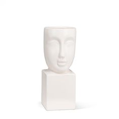 a white ceramic sculpture with a face on it's base, against a white background