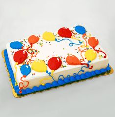 a birthday cake decorated with balloons and confetti on a white tablecloth background