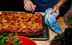 a woman is cutting into a large casserole on a pan with a knife