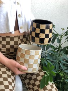 a woman sitting on a bench holding a coffee cup in her hand and potted plant behind her